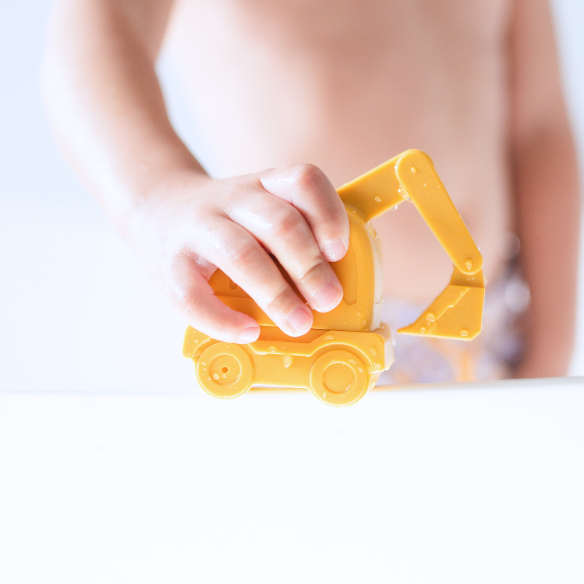 Child playing with a yellow excavator from the Bug + Bean Kids mold-free silicone bath toy set.