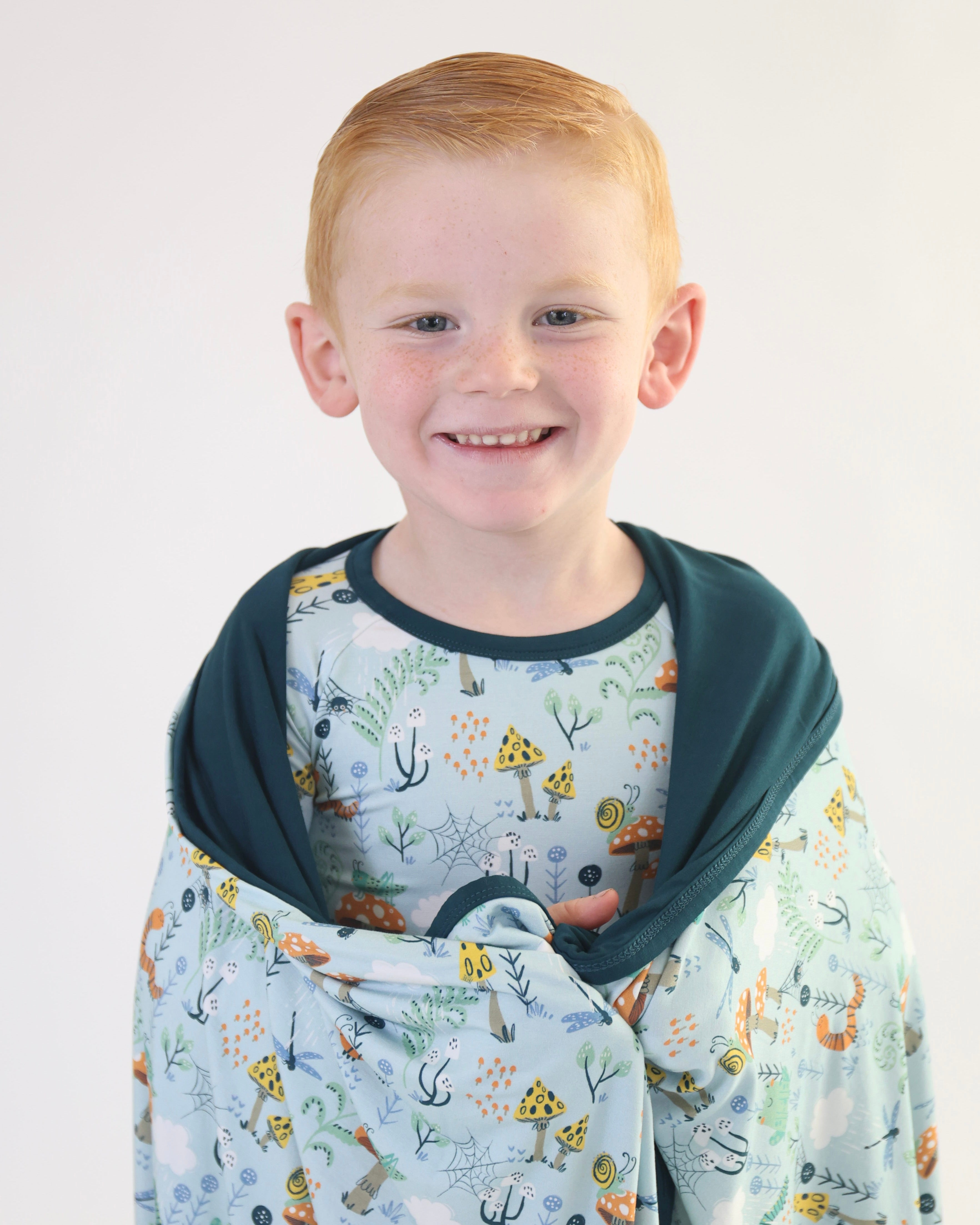 Smiling boy wrapped in Critter Hollow Rainn Cozy Blanket, enjoying its soft and snuggly bamboo fabric.