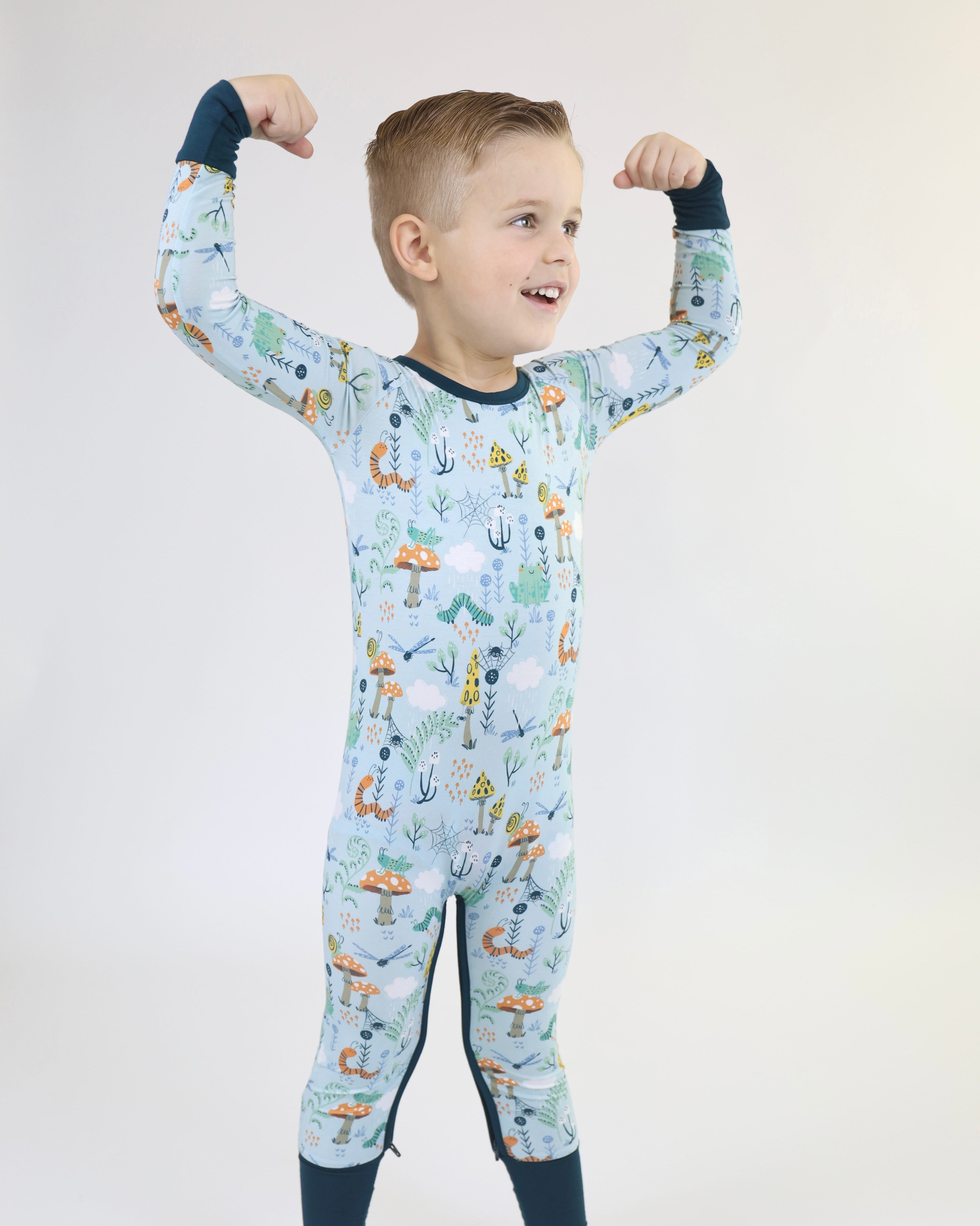 Boy flexing muscles in playful Critter Hollow Crescent Zipp Jammies, showcasing fun animal designs and vibrant colors.