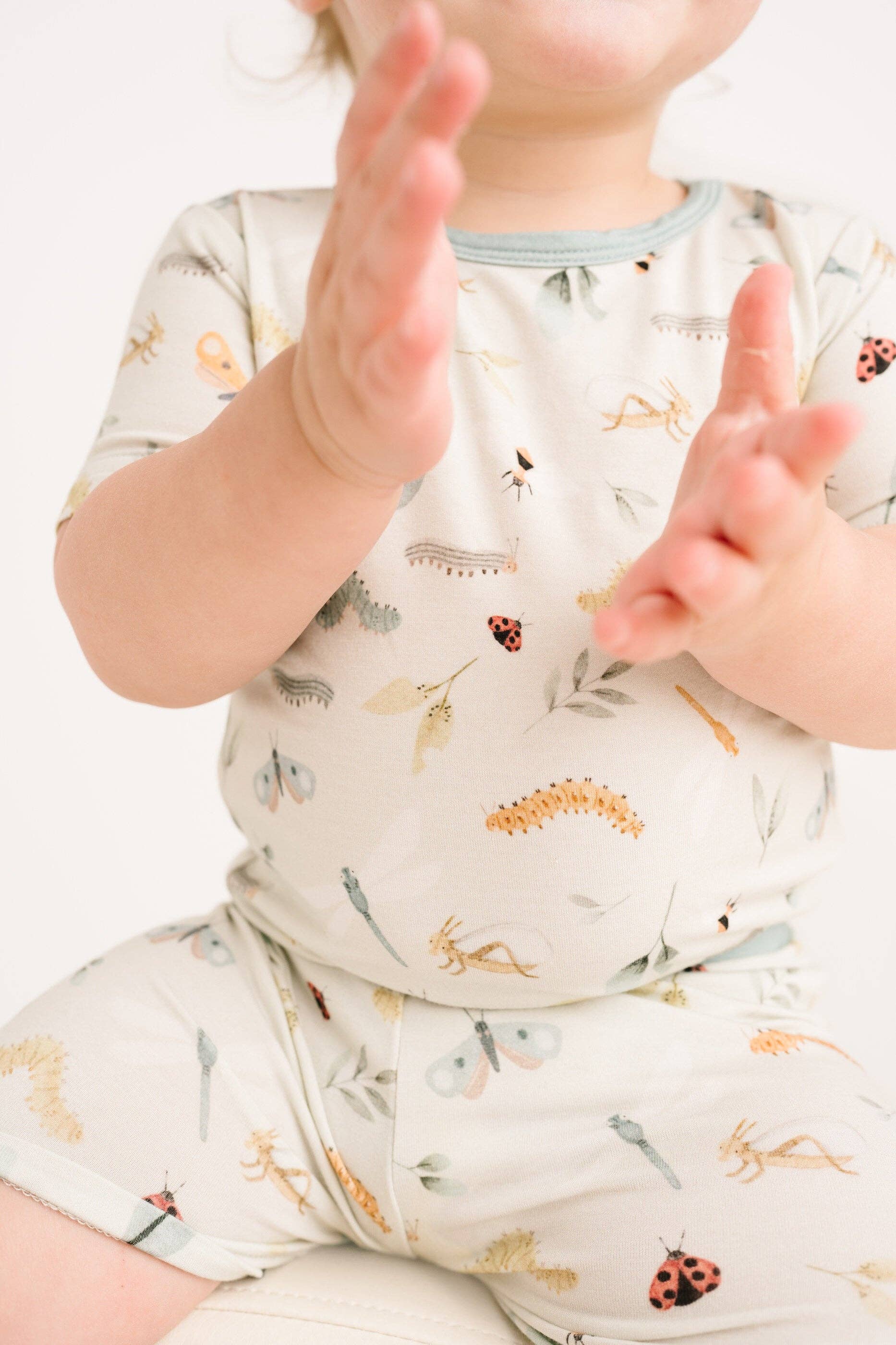 Toddler wearing Bug Buddies Bamboo Shorts Set, clapping hands in bug print outfit from Little One Shop for ages 12-18 months.