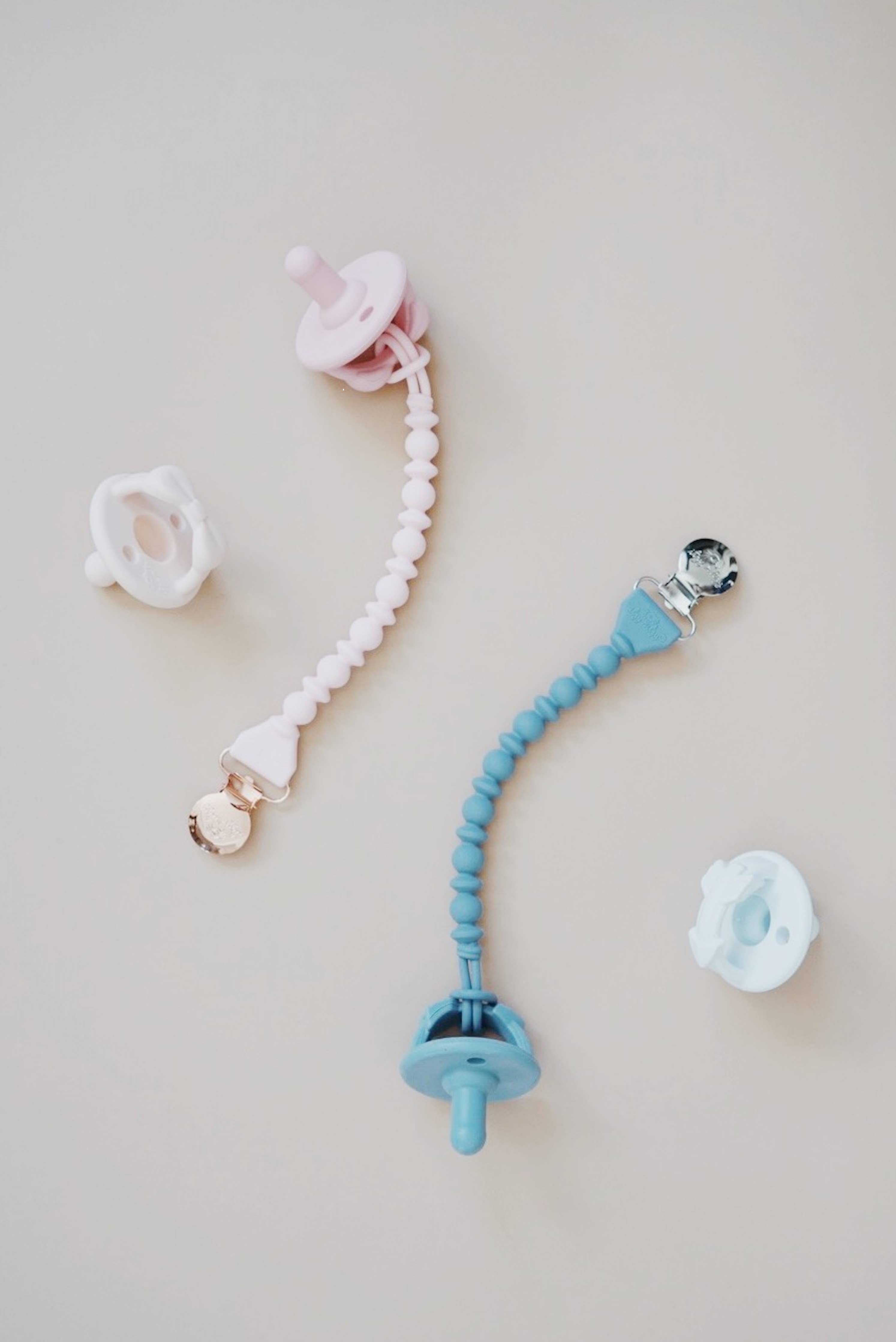 Stylish Sweetie Strap™ silicone pacifier clips in pink and blue, keeping pacifiers secure and looking cute.