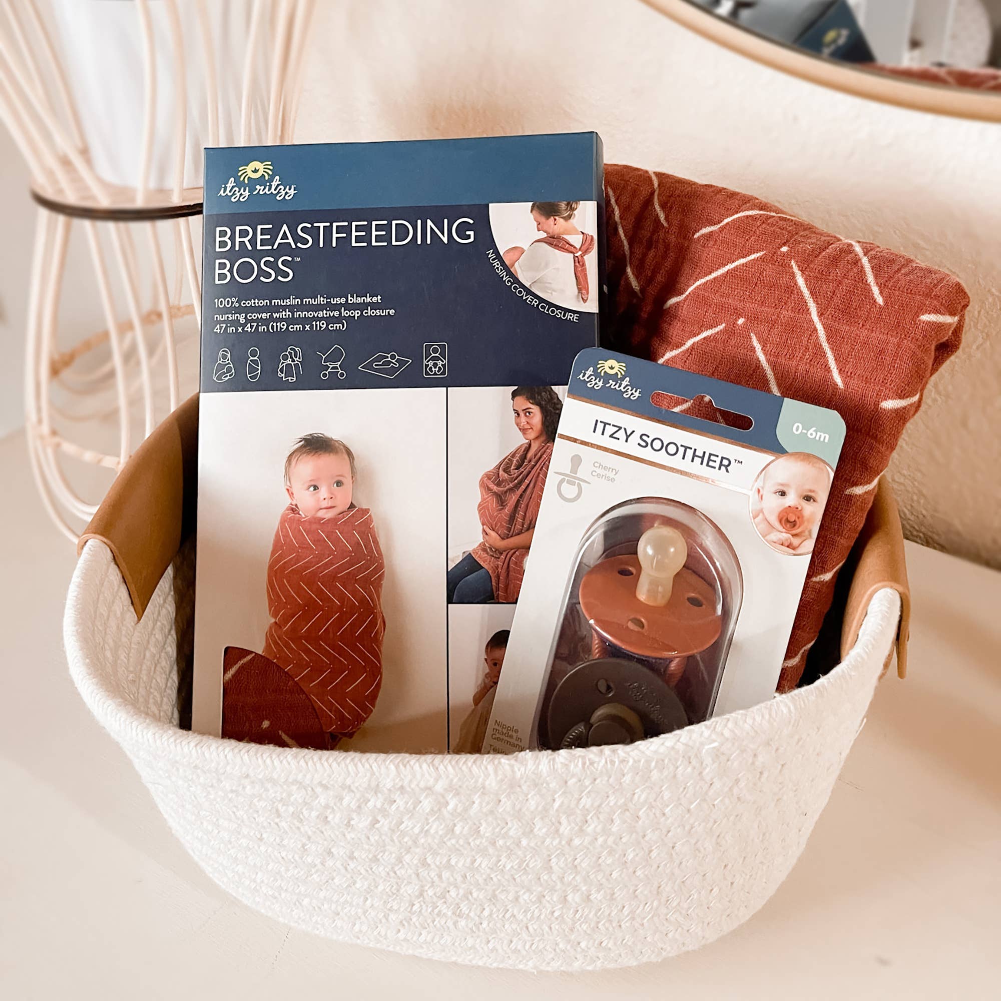 Itzy Ritzy Breastfeeding Boss™ in a basket, showcasing a nursing cover and pacifier, perfect for new parents.