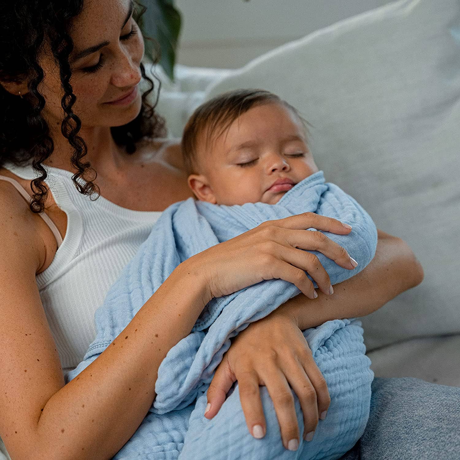 Mom cradles a sleeping baby in a soft blue muslin cotton blanket, showcasing comfort and tenderness.