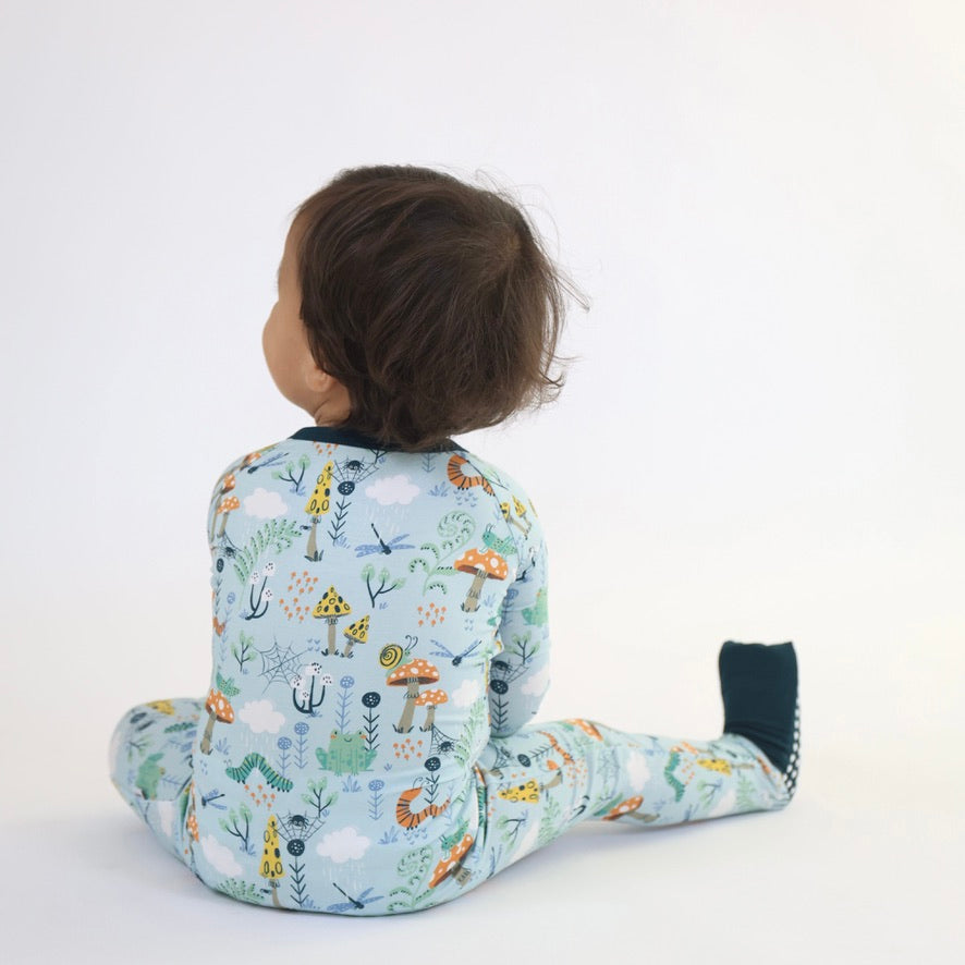 Toddler in Bamboo Zipp Jammies - Critter Hollow with animal print, sitting on white background, showcasing hypoallergenic, breathable material.