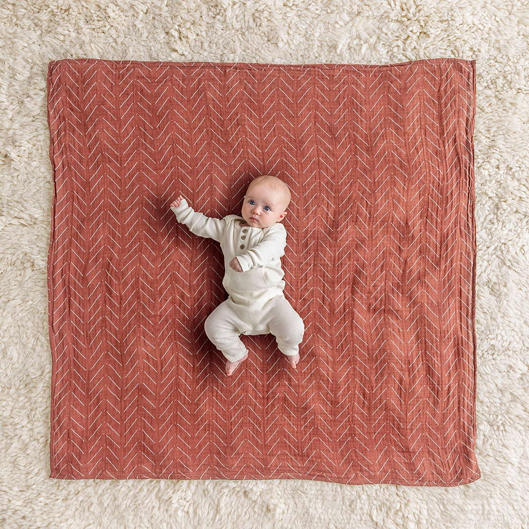 Baby on a soft, rust-colored muslin blanket, showcasing the versatile Itzy Ritzy Breastfeeding Boss™.