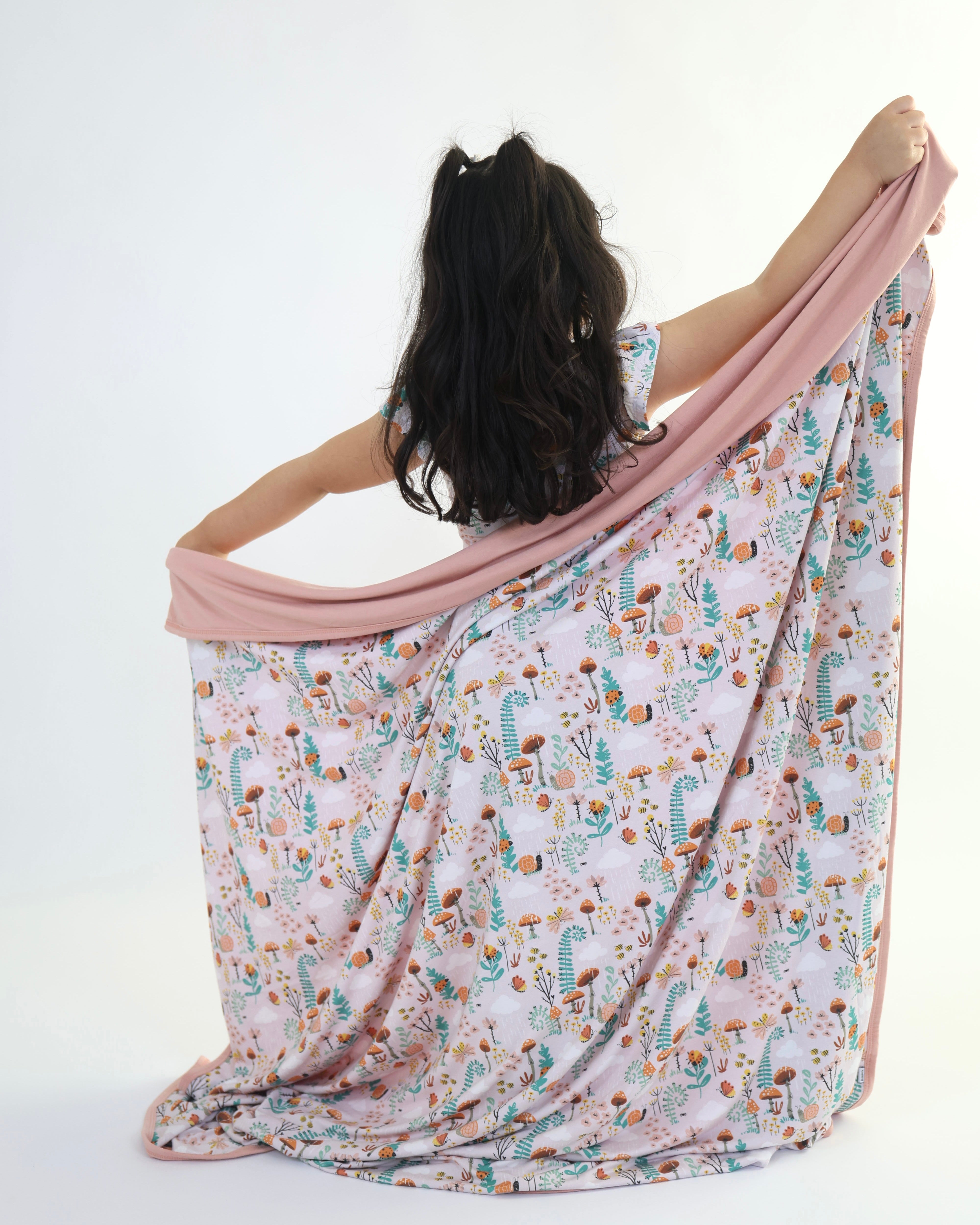 Child holding a colorful Bamboo Blanket - Rainn Cozy - Fern, showcasing its breathable material and eco-friendly design.