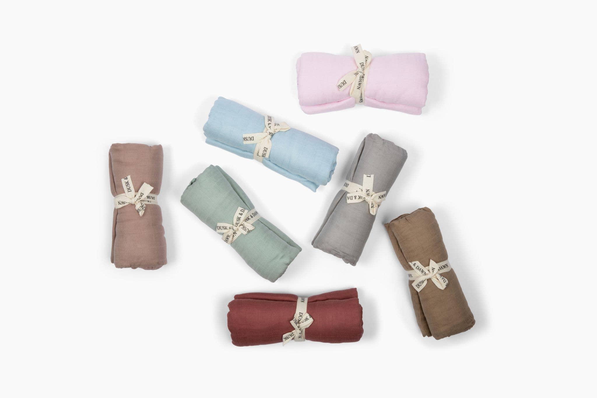 Colorful bamboo muslin baby swaddles in various shades, including sage, pink, and blue, rolled and tied with ribbon, eco-friendly fabric gifts.