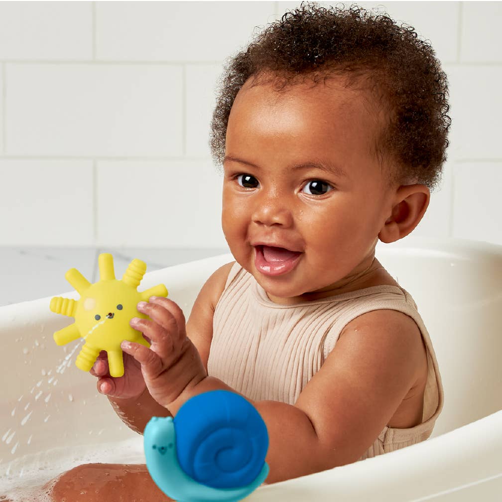 Happy baby in a bath playing with colorful Itzy Splash soft bath toys for fun water adventures.