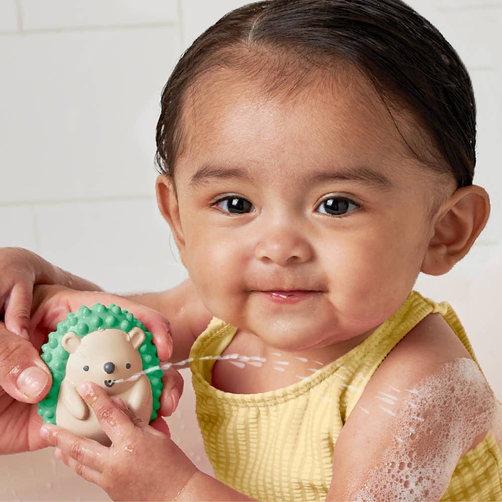 Happy baby playing with soft hedgehog bath toy from Itzy Splash Gift Set™, making bath time fun and engaging.