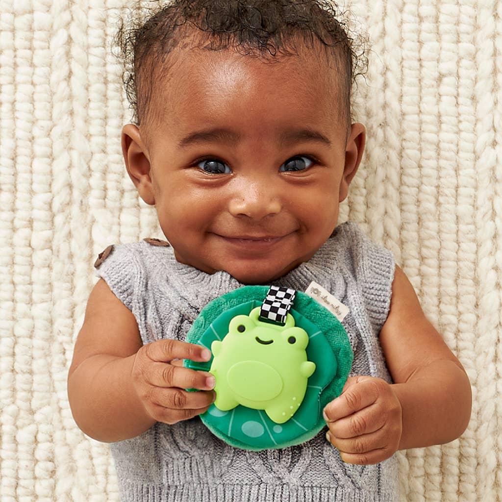 Smiling baby holding Itzy Frog Sweetie Crinkle™ teether, enjoying soothing silicone and plush fun.