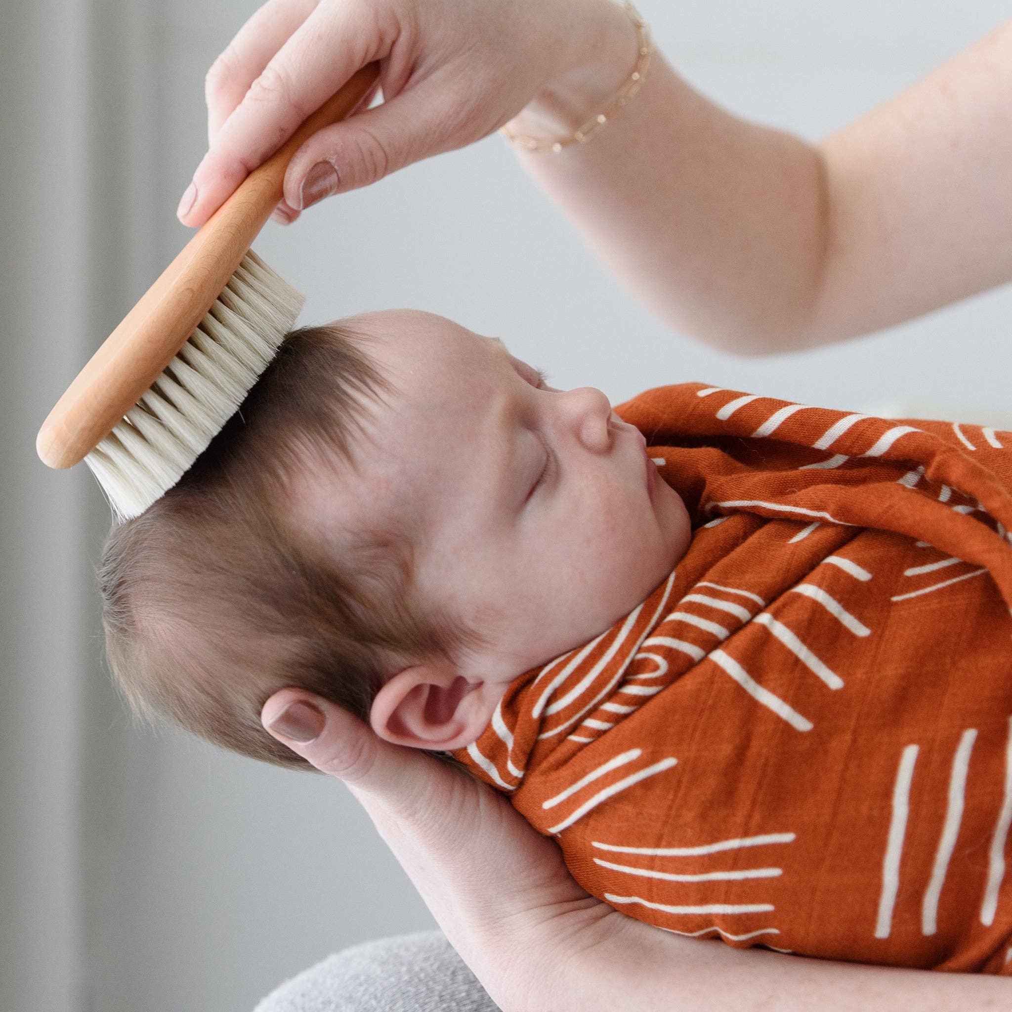 Gentle baby brushing with boho-style Coco Stripes Terra swaddle from the Deluxe Newborn Gift Set, made of bamboo and cotton.