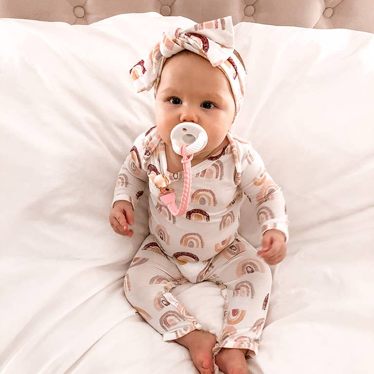 Adorable baby in rainbow outfit with Sweetie Strap™ pacifier clip, showcasing style and functionality.