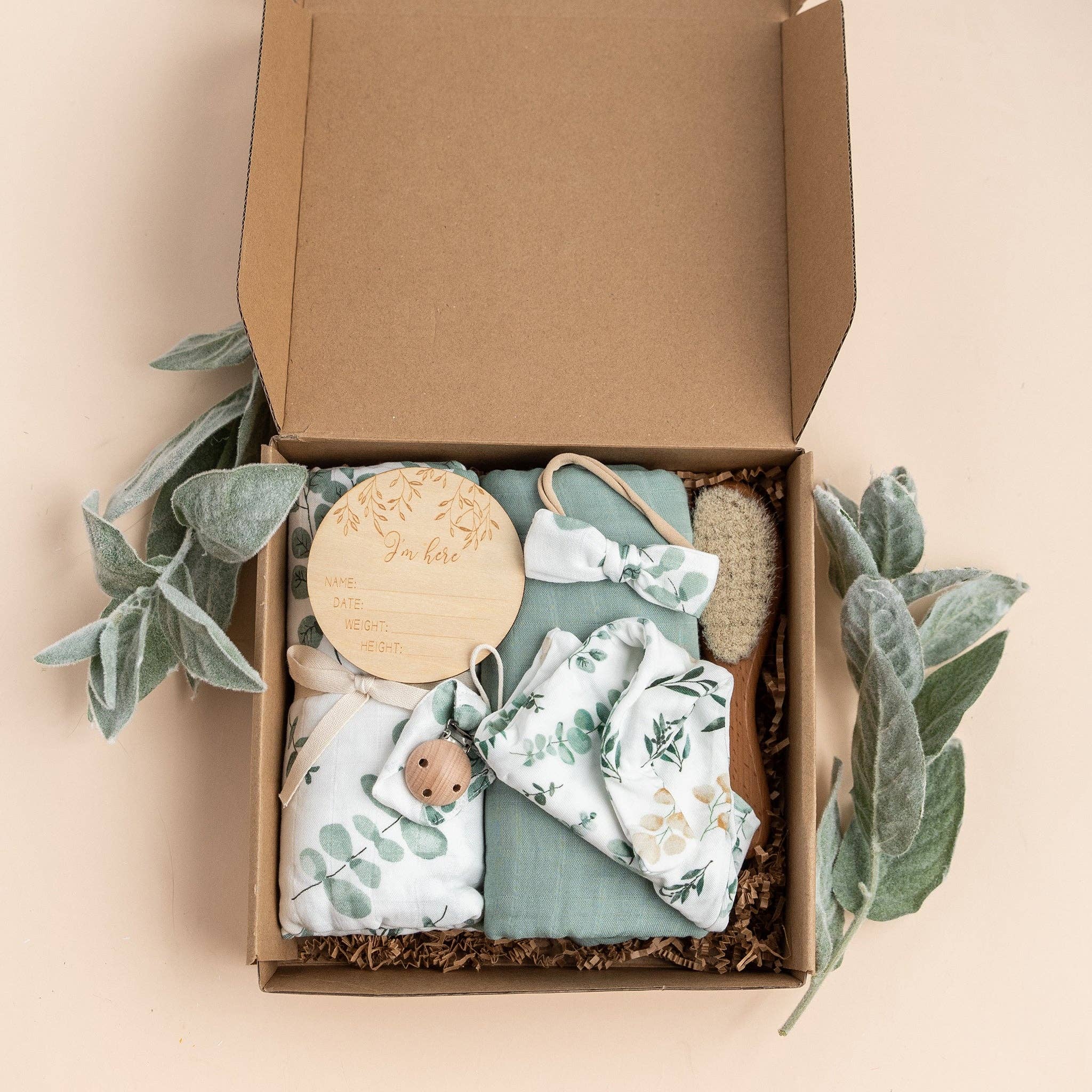 Eucalyptus-themed baby shower gift set in a box with neutral colors, featuring bamboo and cotton blend items. Perfect for new parents.