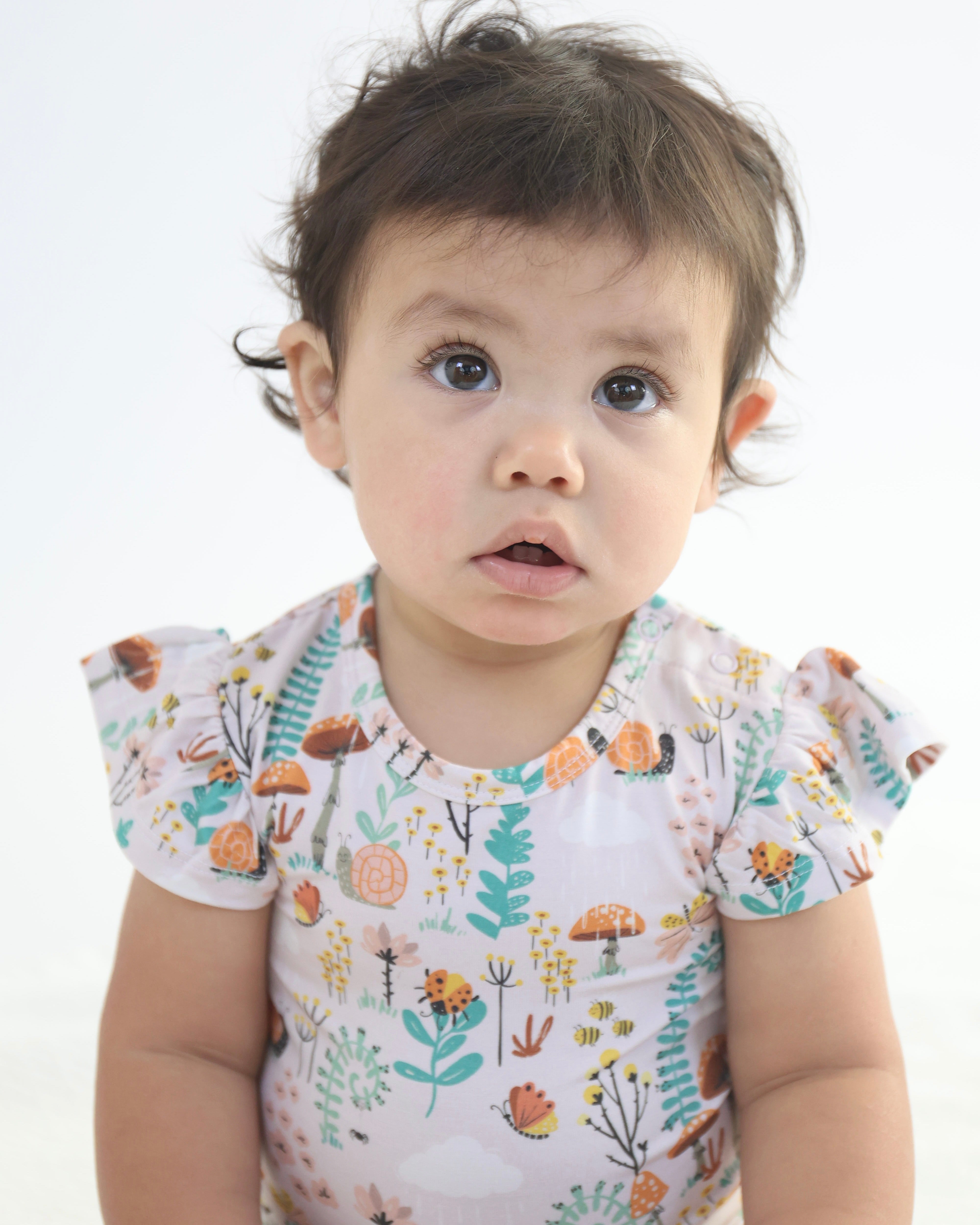 Baby girl in a floral Ruffle Snappy outfit by Rainn, showcasing vibrant nature-inspired prints.