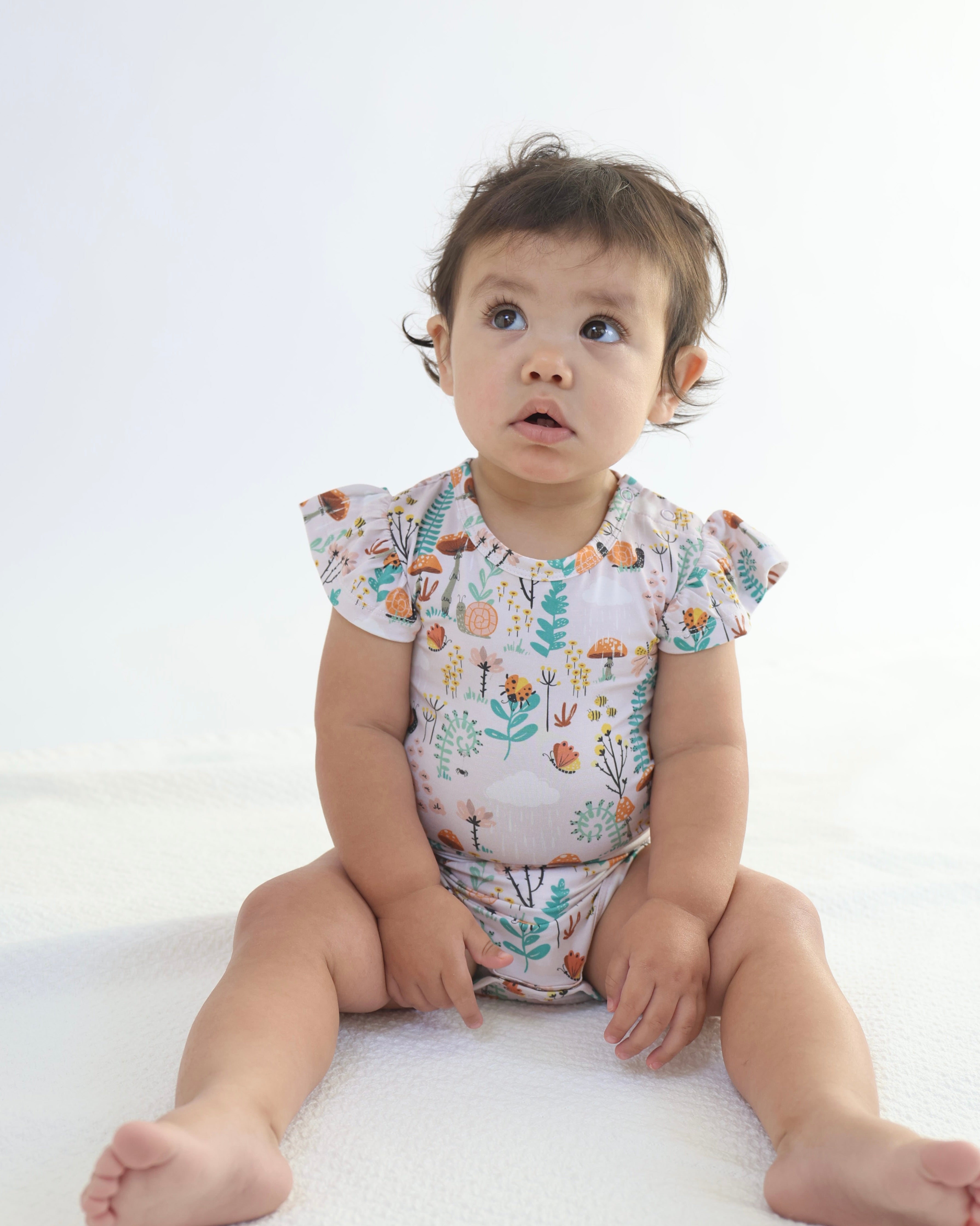 Adorable baby in a floral ruffle bodysuit, showcasing the soft and breathable bamboo fabric by Rainn.