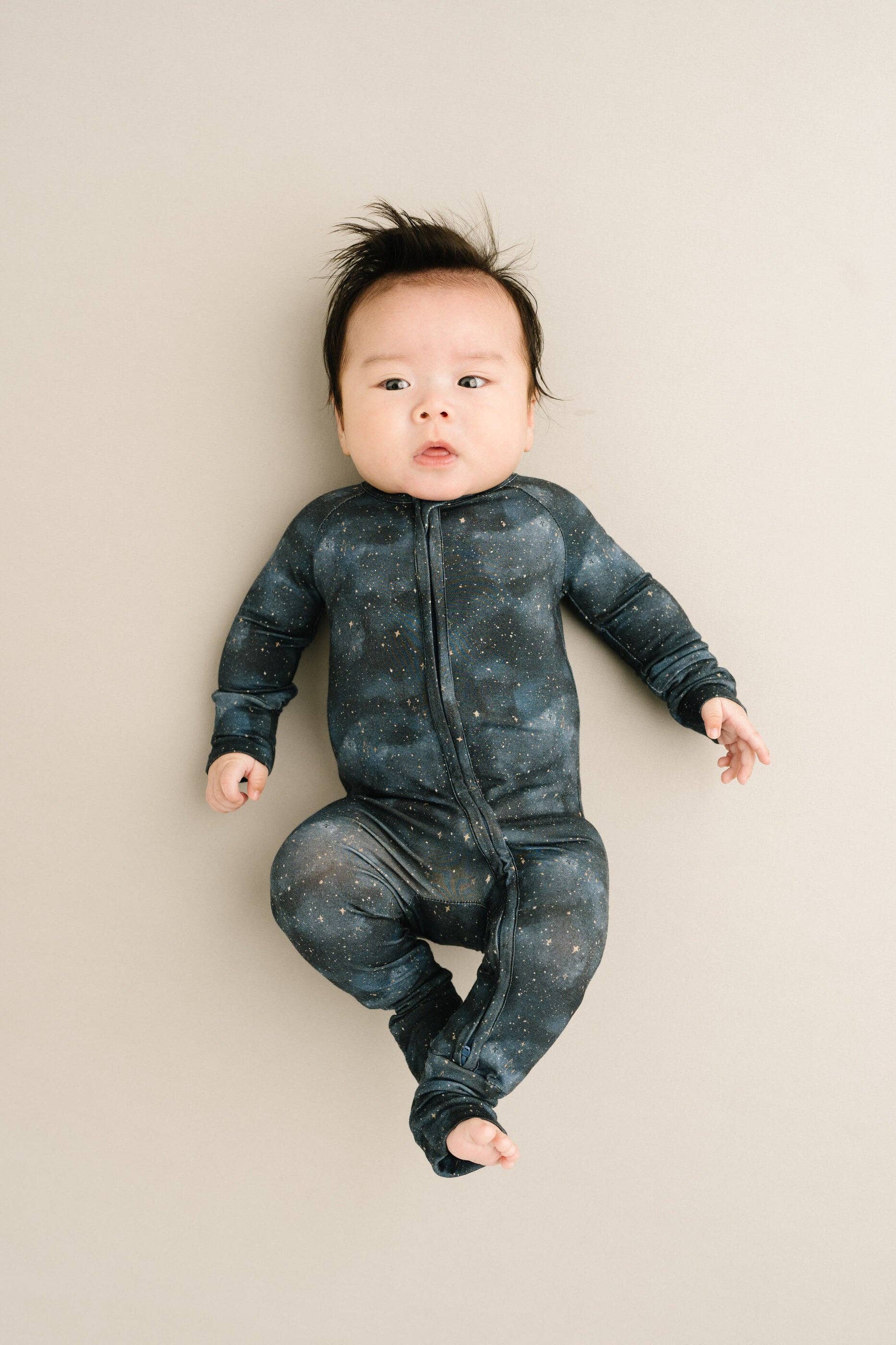 Baby wearing Moonlight Bamboo Sleeper from Little One Shop, 6-12M, in navy with star pattern, lying on a neutral background.