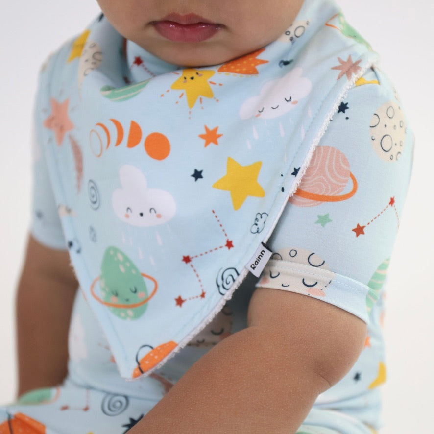 Baby wearing Cosmic Bandana Dribble Bib, featuring colorful planets and stars for drool protection and style.