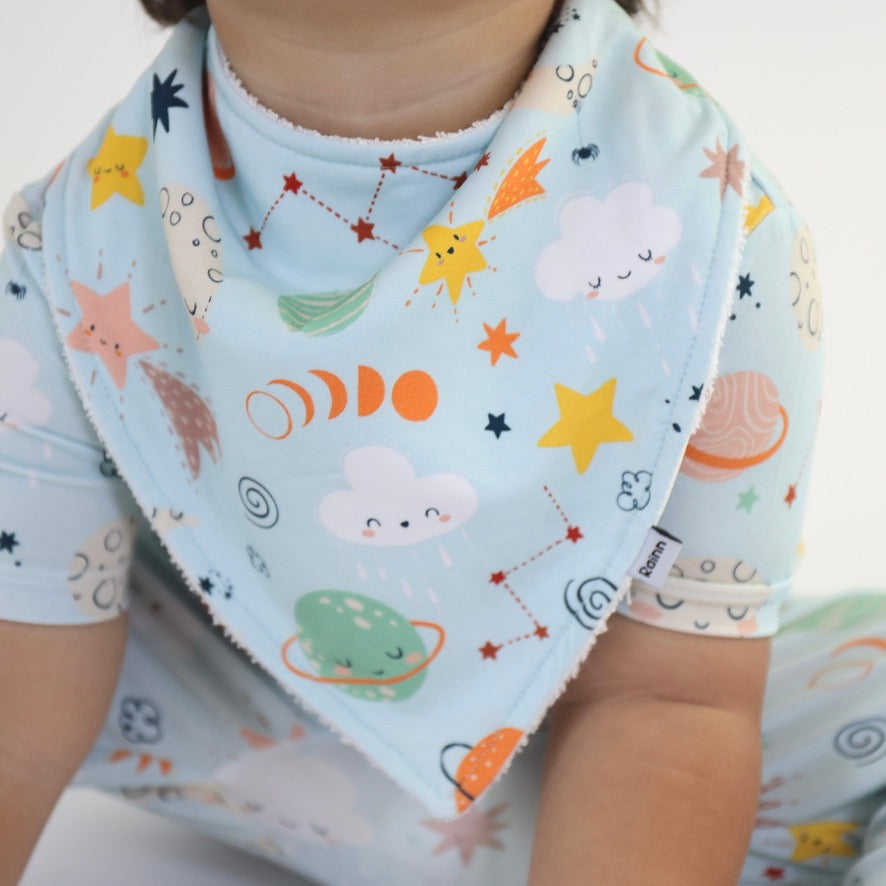 Child wearing Cosmic Bandana Dribble Bib featuring colorful space-themed prints by Rainn, perfect for drooling babies.