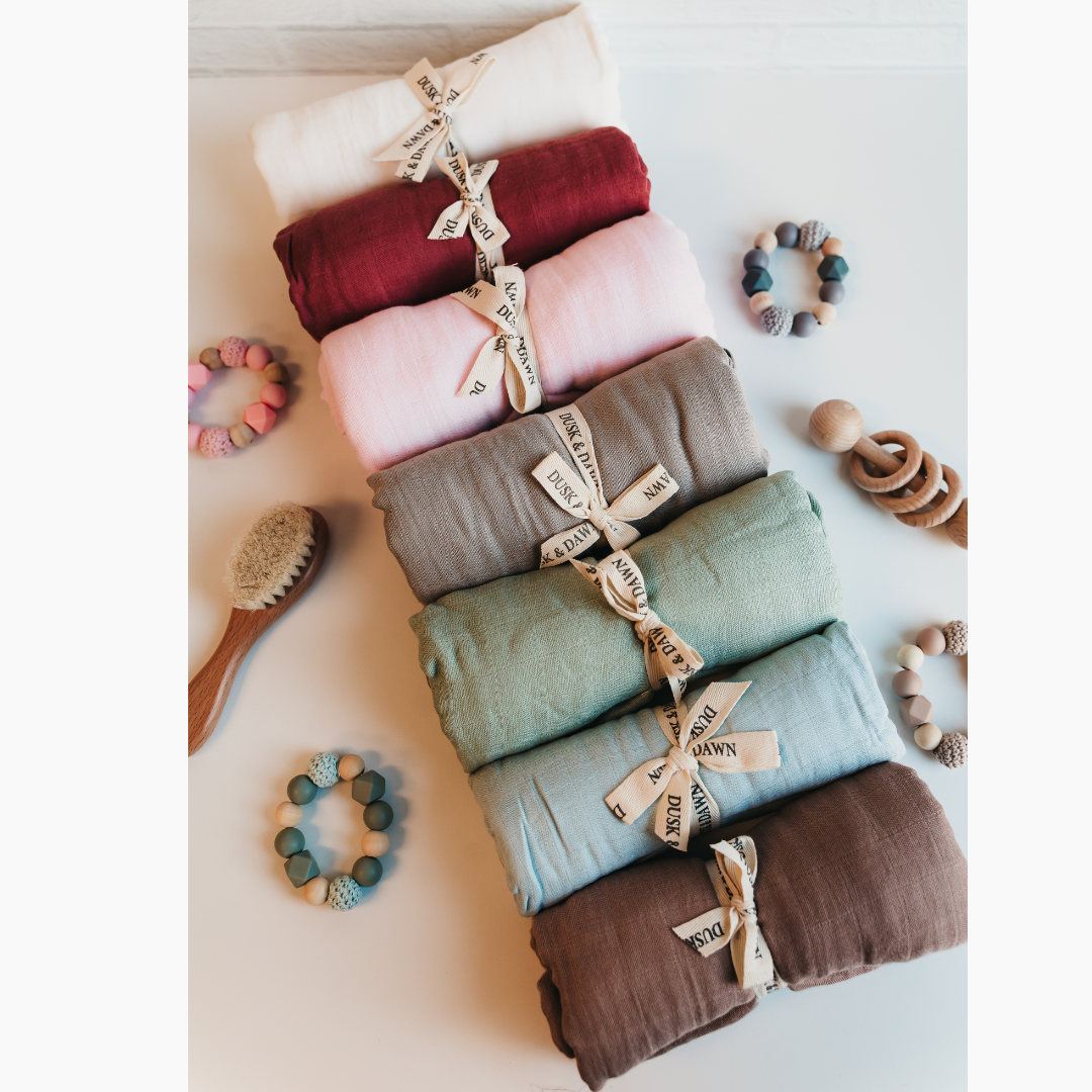 Stack of colorful bamboo muslin baby swaddles with accessories by Giften Market, showcasing soft, breathable, eco-friendly baby wraps.
