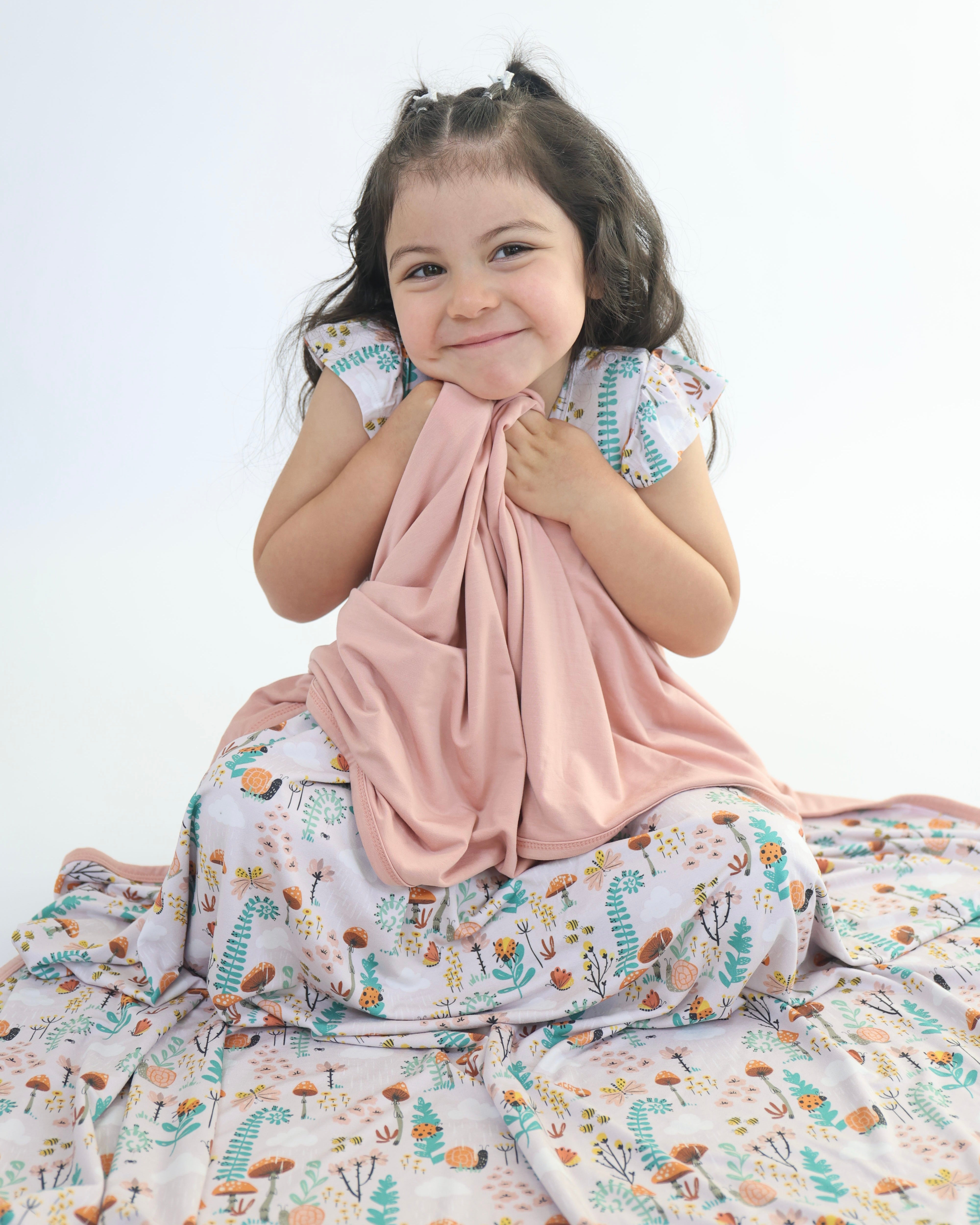 Child cuddling pink Bamboo Blanket with nature-themed design, highlighting comfort and breathability for sensitive skin.